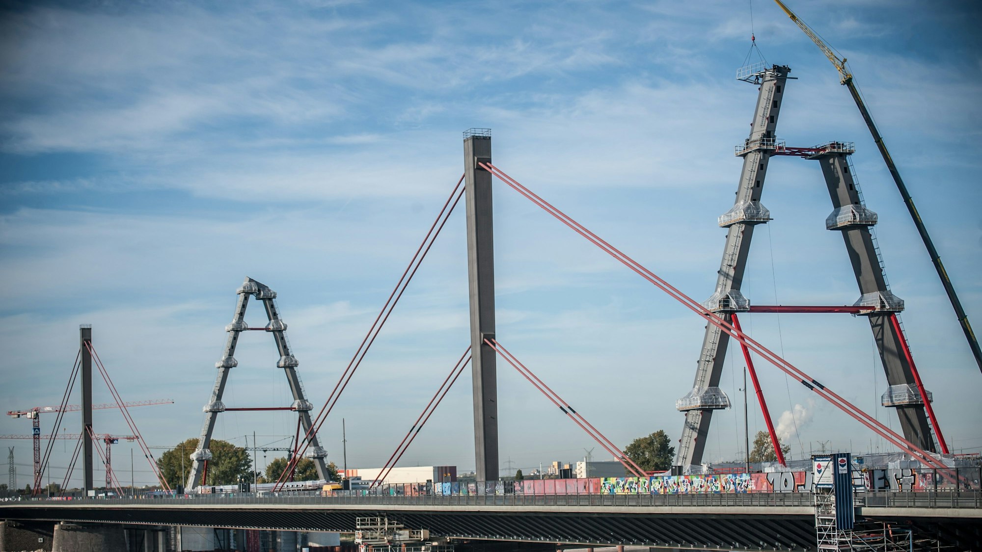 Die neue Rheinbrücke für die Autobahn 1 zwischen Köln und Leverkusen im Oktober 2022. Ein Pylon steht, ein zweiter wird gerade aufgebaut. Dazu hängt ein Kran eine Arbeitsplattform ein.