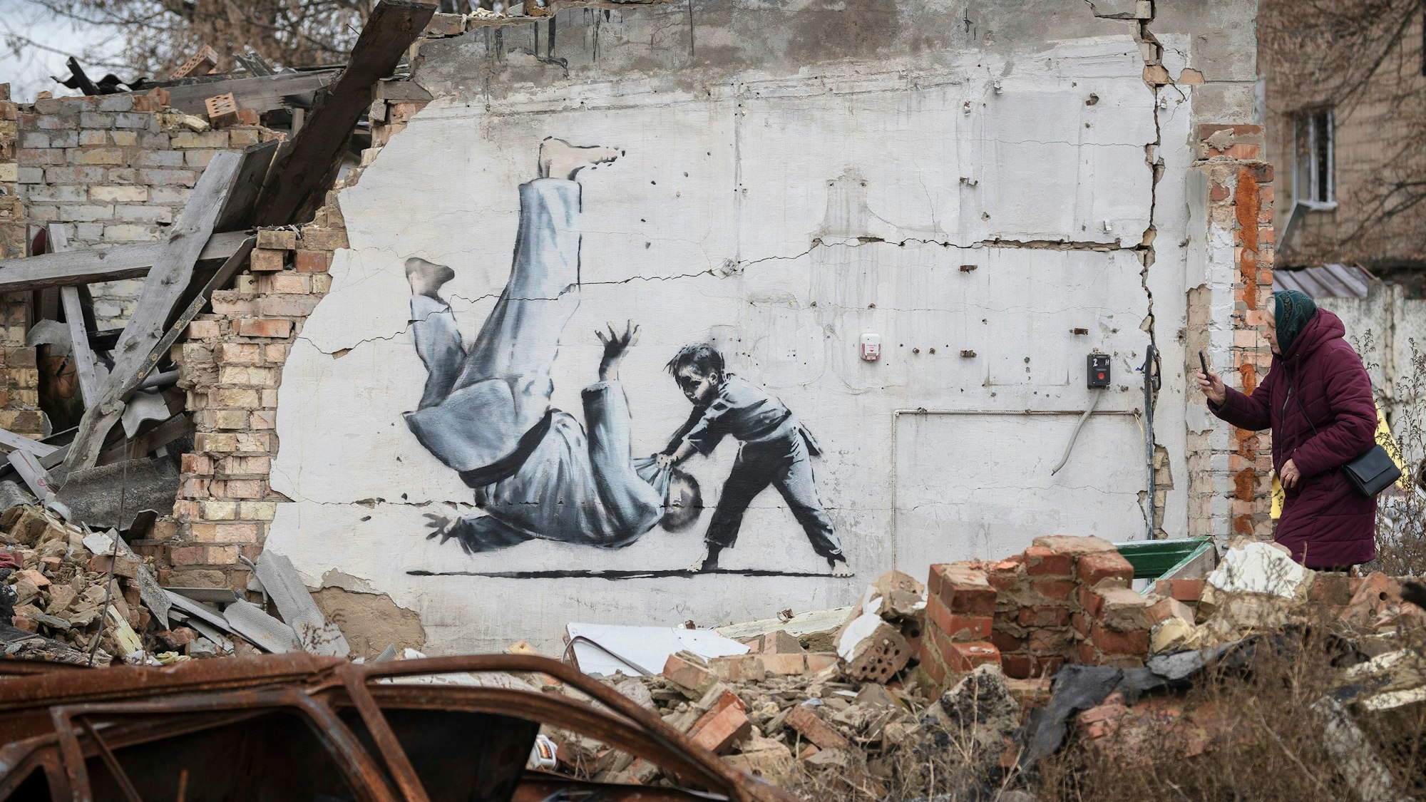 Eine ukrainische Frau fotografiert ein Kunstwerk, das möglicherweise vom britischen Straßenkünstler Banksy an einem durch Kämpfe zerstörten Gebäude in Borodyanka angefertigt wurde.