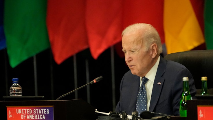 Das Foto zeigt den US-Präsident Joe Biden während des G20-Gipfels. Er spricht in ein Mikrofon, hinter ihm befinden sich Flaggen.