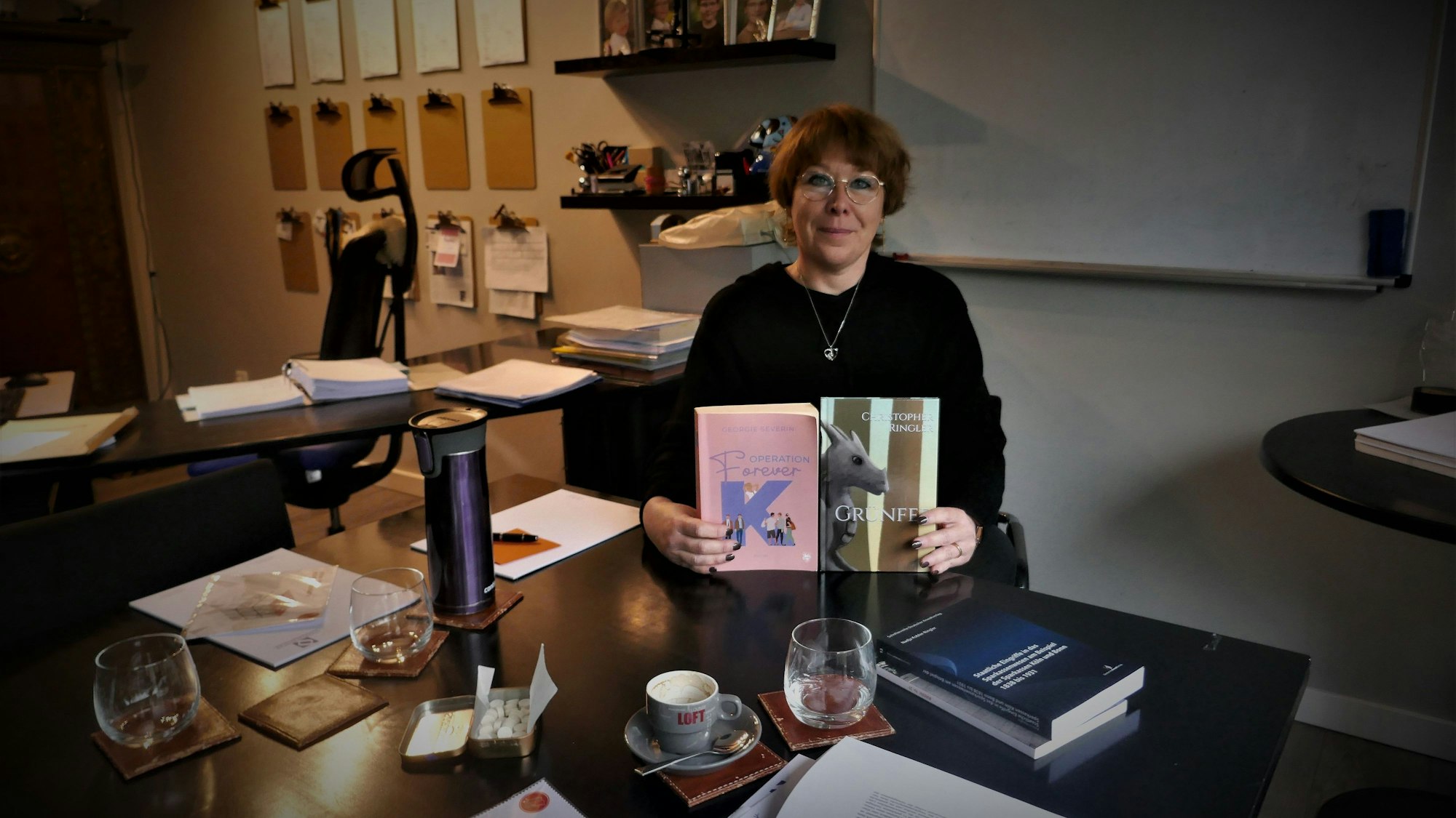 Die Autorin Nadja Kobler-Ringler, alias Georgie Severin, sitzt an einem Schreibtisch und zeigt zwei Bücher, ihr eigenes und das ihres Sohnes Christopher.