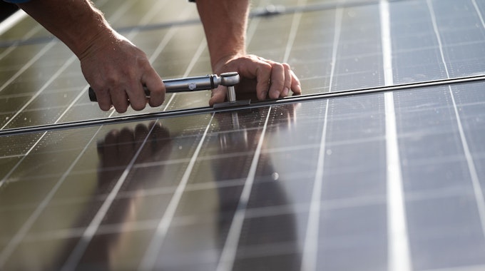 Ein Mitarbeiter montiert Photovoltaikmodule auf dem Dach eines Wohnhauses.