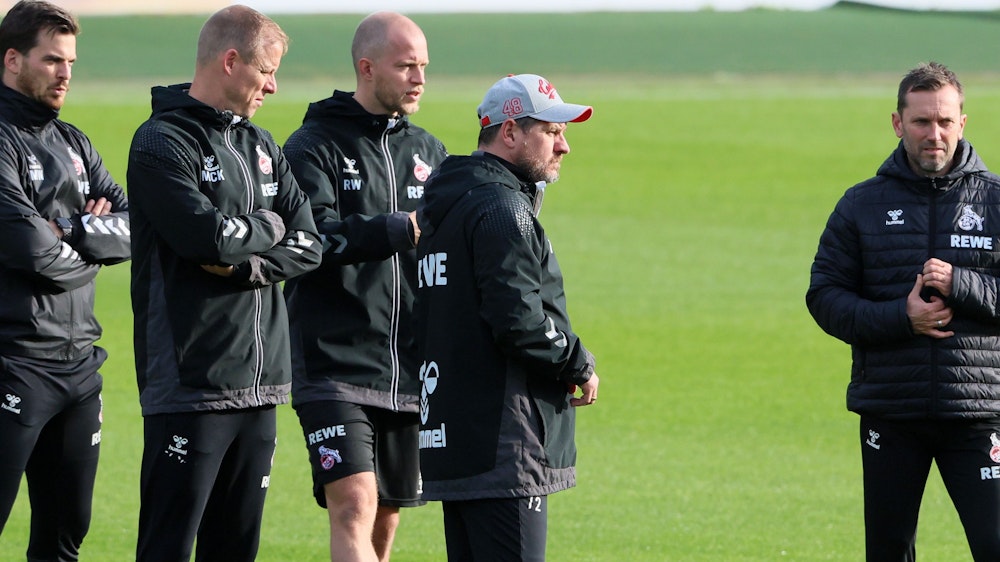 Steffen Baumgart steht mit seinen Assistenten André Pawlak, René Wagner und Kevin McKenna sowie dem Athletiktrainer Max Weuthen auf dem Trainingsplatz des 1. FC Köln.