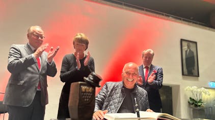 Rolly Brings wird mit dem Karl-Küpper-Preis ausgezeichnet und trägt sich ins Goldene Buch der Stadt Köln ein. Im Hintergrund applaudieren OB Henriette Reker, Festkomitee-Präsident Christoph Kuckelkorn und Bernhard Conin.&nbsp;