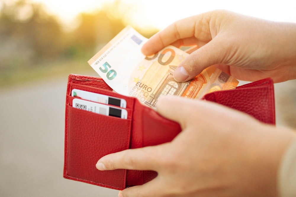 Frau hält einen 50-Euro-Schein und eine rote Geldbörse in der Hand.