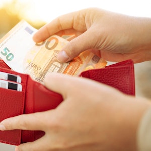 Frau hält einen 50-Euro-Schein und eine rote Geldbörse in der Hand.