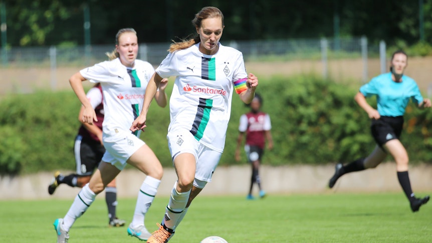 Sarah Schmitz, Spielführerin der Frauenmannschaft von Borussia Mönchengladbach, läuft mit dem Ball am Fuß. Am Arm trägt sie eine regenbogenfarbene Kapitänsbinde.