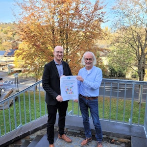 Bürgermeister Ingo Pfennings (l.) und Musikschulleiter Bernhard Vorhagen präsentieren auf einer Treppe das Plakat für das Festkonzert 50 Jahre Musikschulzweckverband Schleiden.
