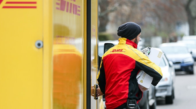 Ein DHL-Paketzusteller verlässt mit mehreren Sendungen sein Fahrzeug.