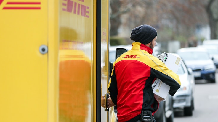 Ein DHL-Paketzusteller verlässt mit mehreren Sendungen sein Fahrzeug.