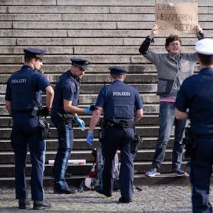 Ein Klimaaktivist steht vor der bayerischen Staatskanzlei und halten ein Schild mit der Aufschrift„&nbsp;Lieber wegsperren als reden“&nbsp; in den Händen. Um ihn herum stehen Polizisten.