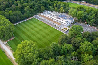 Das Bild zeigt das Clubhaus des 1. FC Köln mit dem Trainingsplatz 1 (vorne) und dem Franz-Kremer-Stadion (hinten rechts) im Äußeren Grüngürtel.