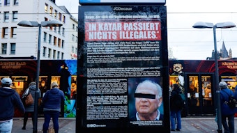 Ein Plakat, das wie ein Zeitungsartikel gestaltet ist, hängt in einem Schaukasten am Heumarkt unter dem Zeichen für die U-Bahn-Haltestelle. Darauf ist ein Foto von Uli Hoeneß mit einem schwarzen Balken vor den Augen zu sehen.