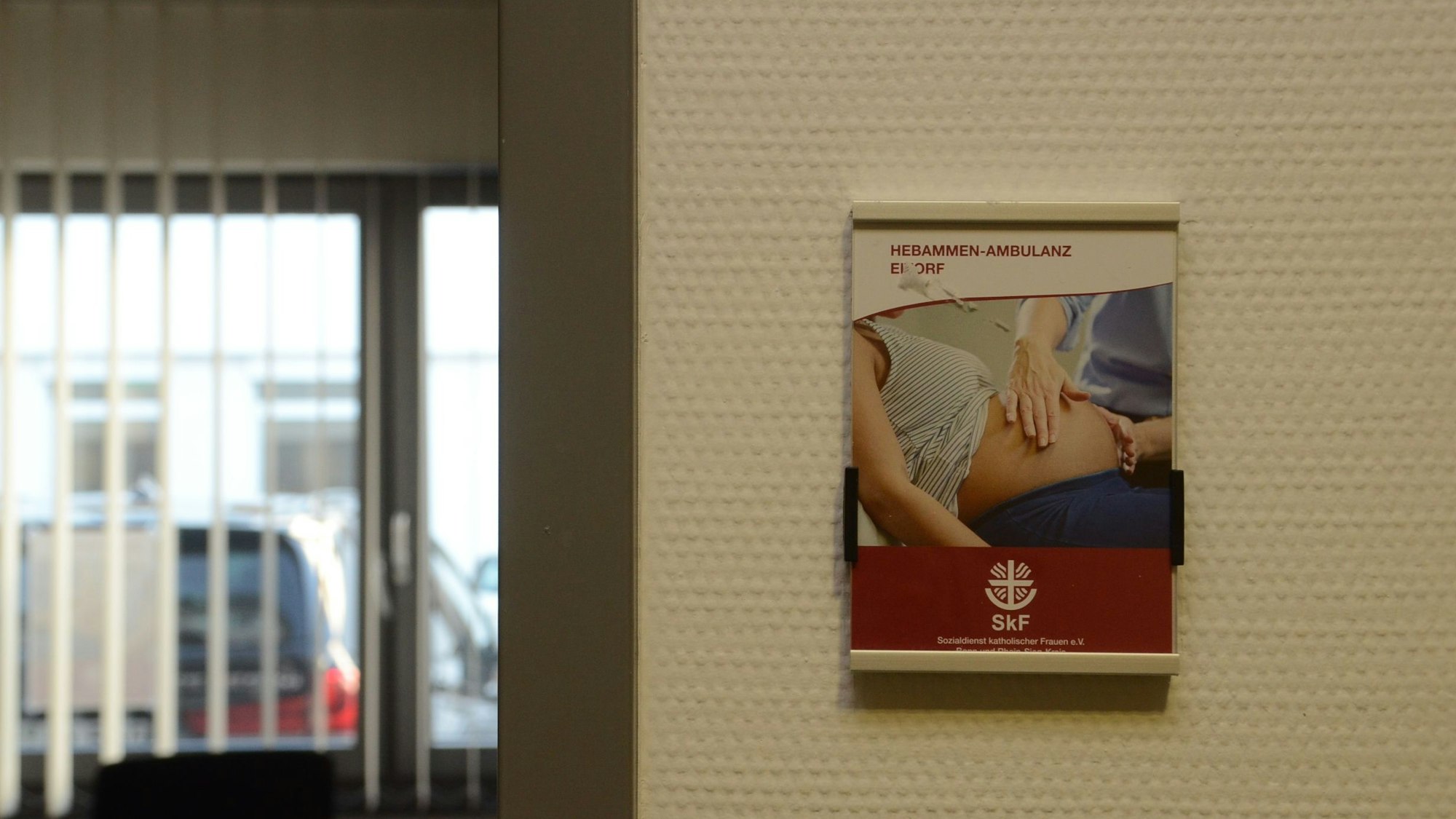 Neben der Tür in ein Beratungszimmer hängt das Plakat mit Werbung für die Hebammenambulanz.