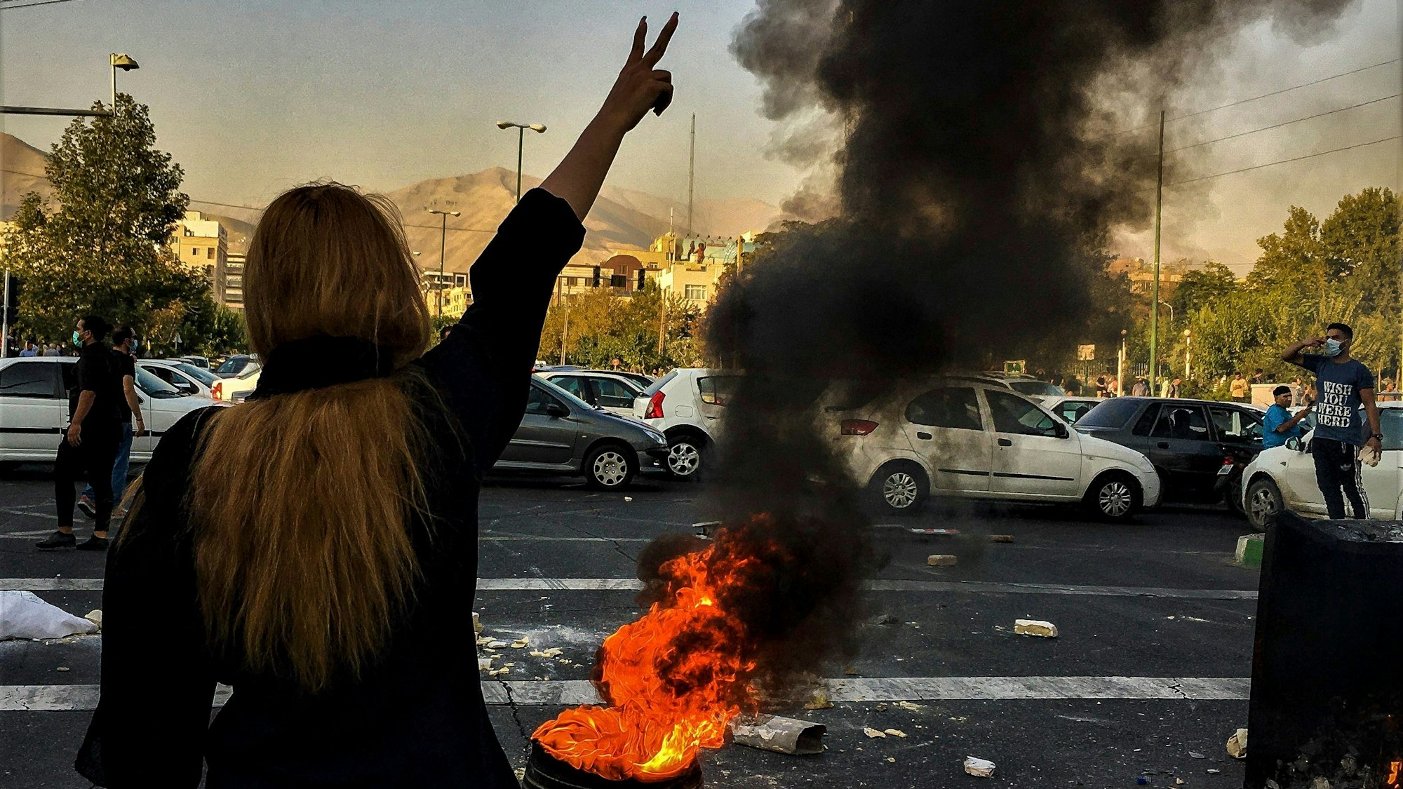 Eine Frau steht während einer Demonstration nach dem Tod der 22-jährigen Jina Amini vor einem brennenden Autoreifen und zeigt das Victory-Zeichen.