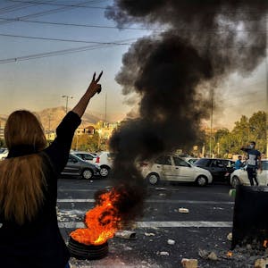 Eine Frau steht während einer Demonstration nach dem Tod der 22-jährigen Jina Amini vor einem brennenden Autoreifen und zeigt das Victory-Zeichen.