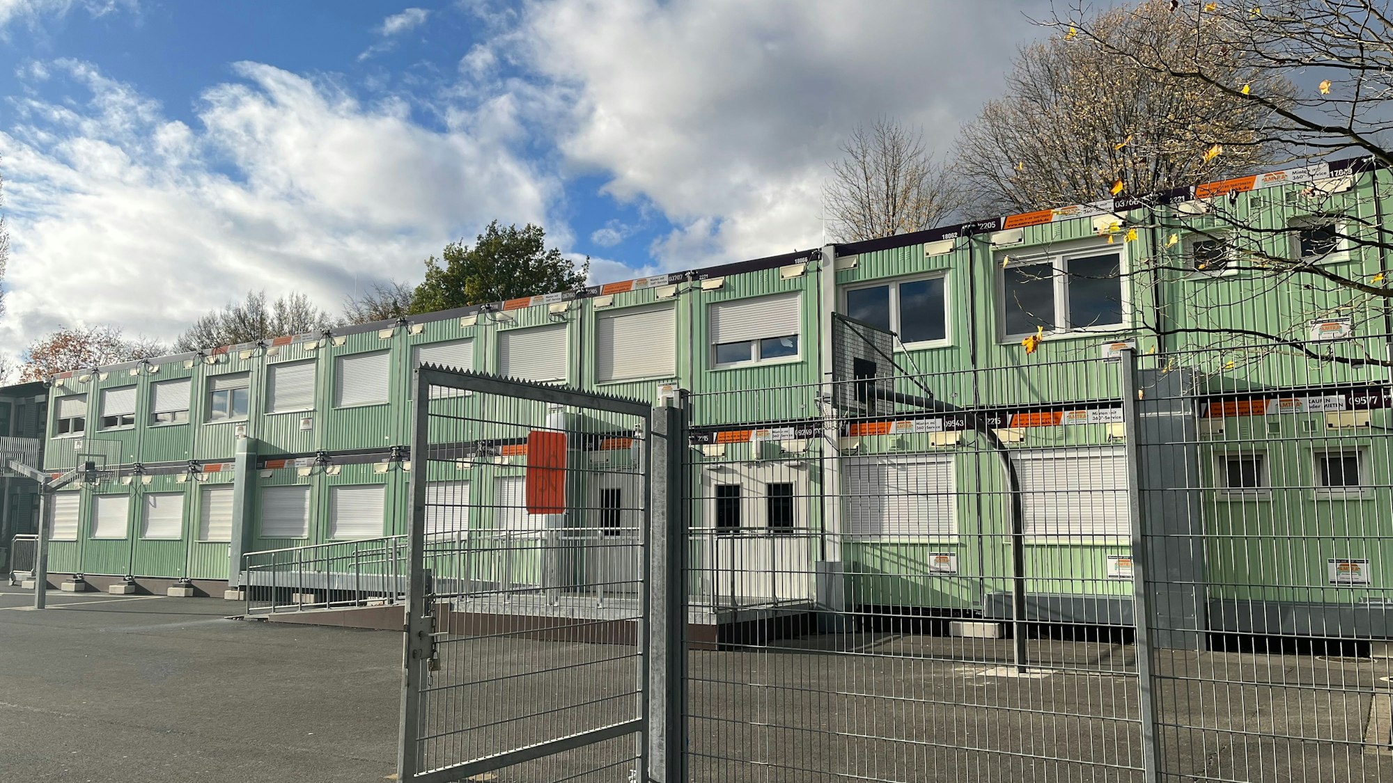 Grüne Container stehen auf einem kargen Schulhof.