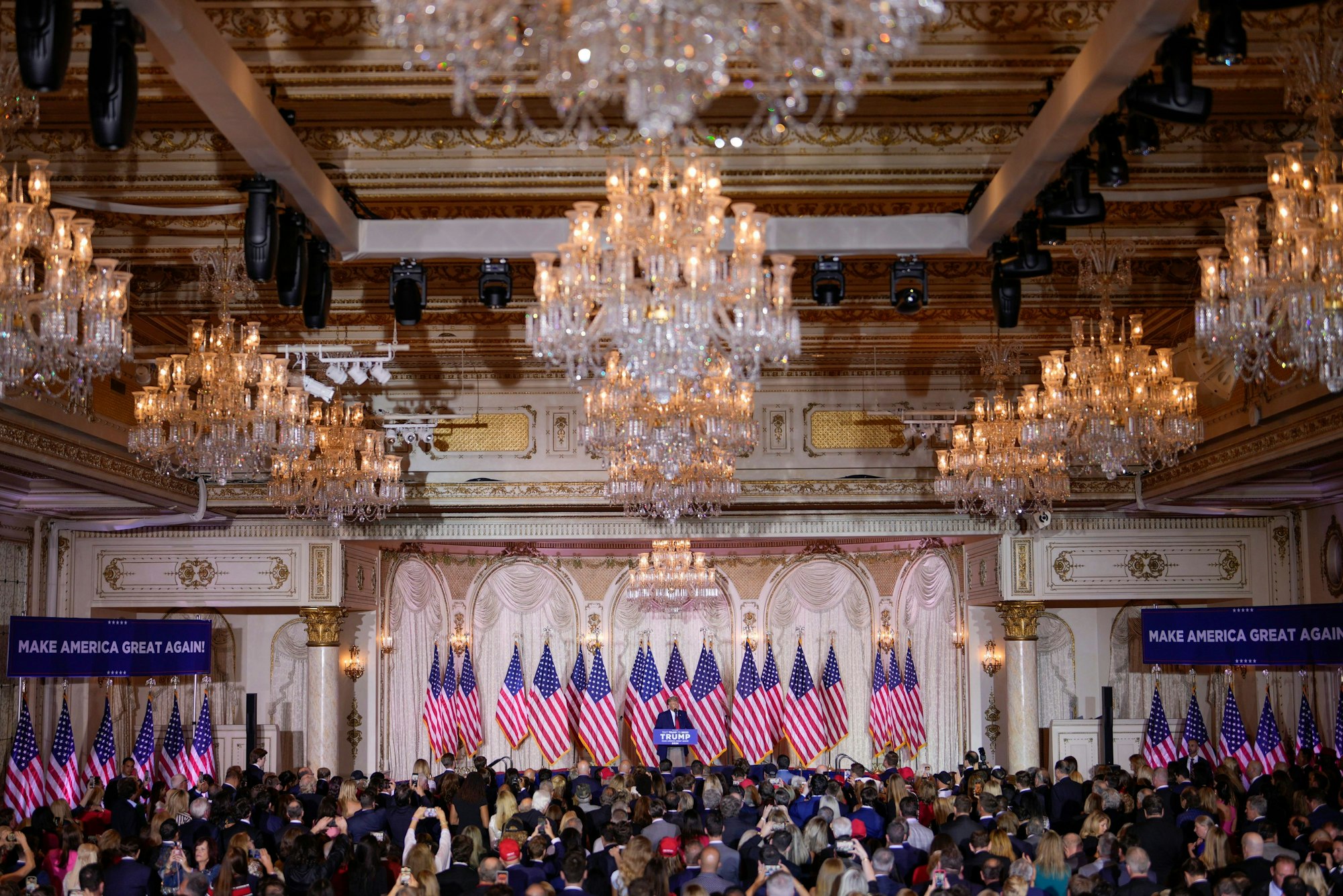 Inszenierung in Trumps Hotel in Florida: ein mit vielen US-Fahnen geschmückter Balsall in Mar-a-Lago. Auf der Bühne ist Donald Trump zu erkennen.