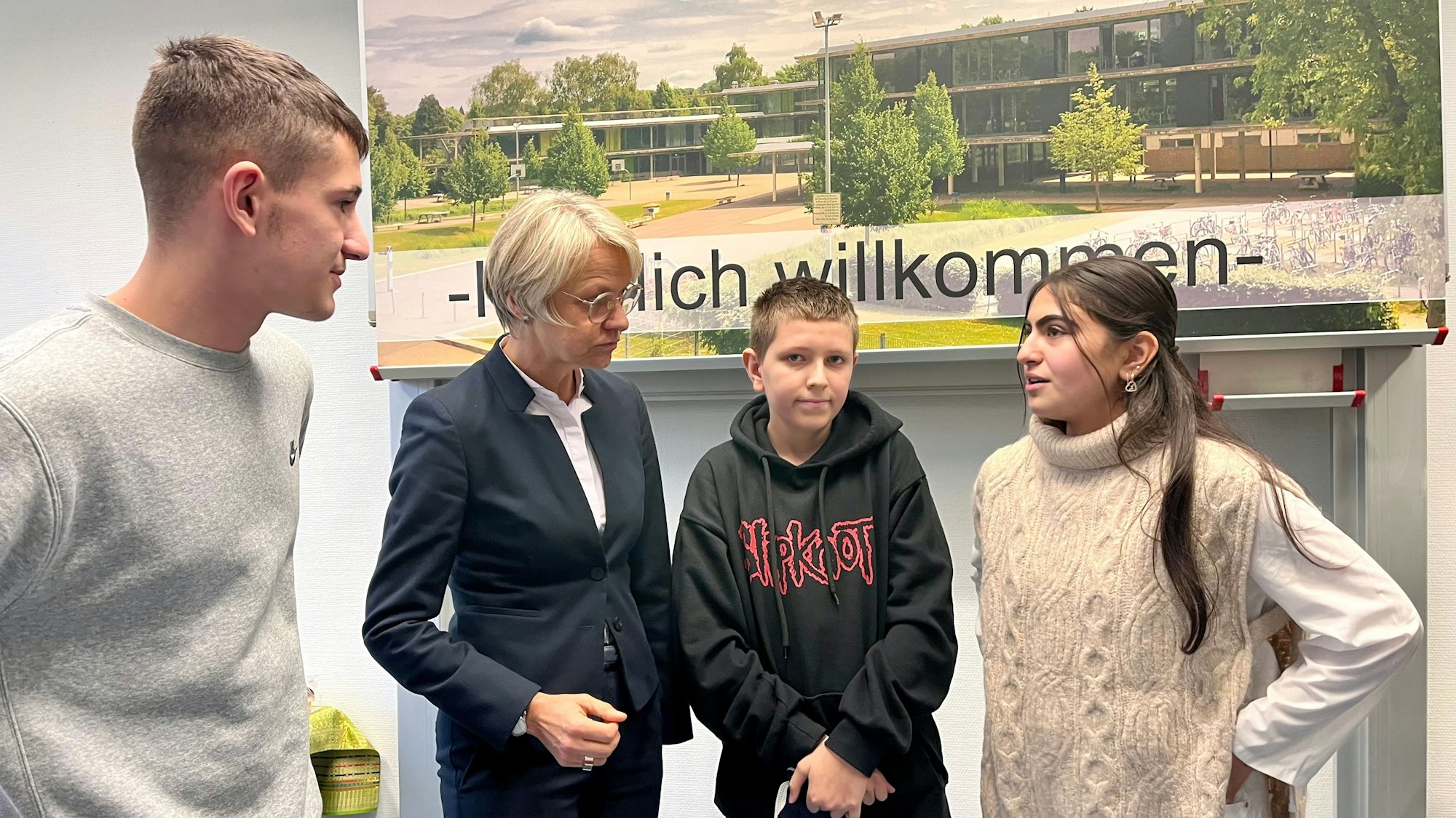 Zwei Schüler und eine Schülerin diskutieren vor einem Plakat der Theodor-Heuss-Realschule mit der Schulministerin Dorothee Feller.