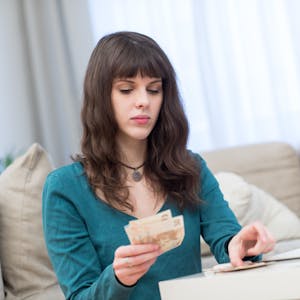 Eine junge Frau sitzt am Couchtisch und zählt Geldscheine.