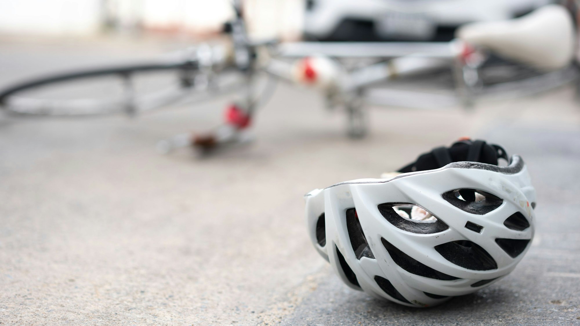 Ein Helm und ein umgefallenes Fahrrad liegen vor einem Auto auf der Straße