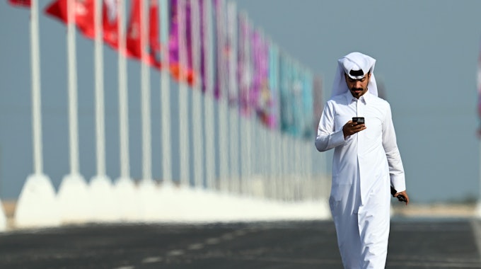 Ein Mann schaut am 17. November 2022 kurz vor dem Start der Fußball-WM in Katar auf sein Handy. Im Hintergrund ist in der Stadt Al Shamal für die WM geschmückt.