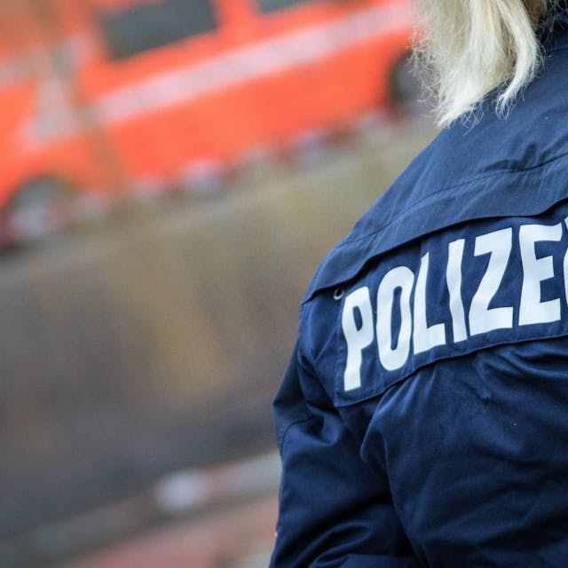 Eine Polizistin auf deren Jacke der Schriftzug „Polizei“ zu sehen ist, steht an einer Einsatzstelle.