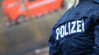 Eine Polizistin auf deren Jacke der Schriftzug „Polizei“ zu sehen ist, steht an einer Einsatzstelle.