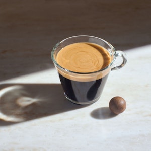 Die gepresste Kaffeekugel als Zero-Waste-Kaffeekapsel liegt neben einer Tasse Kaffee.