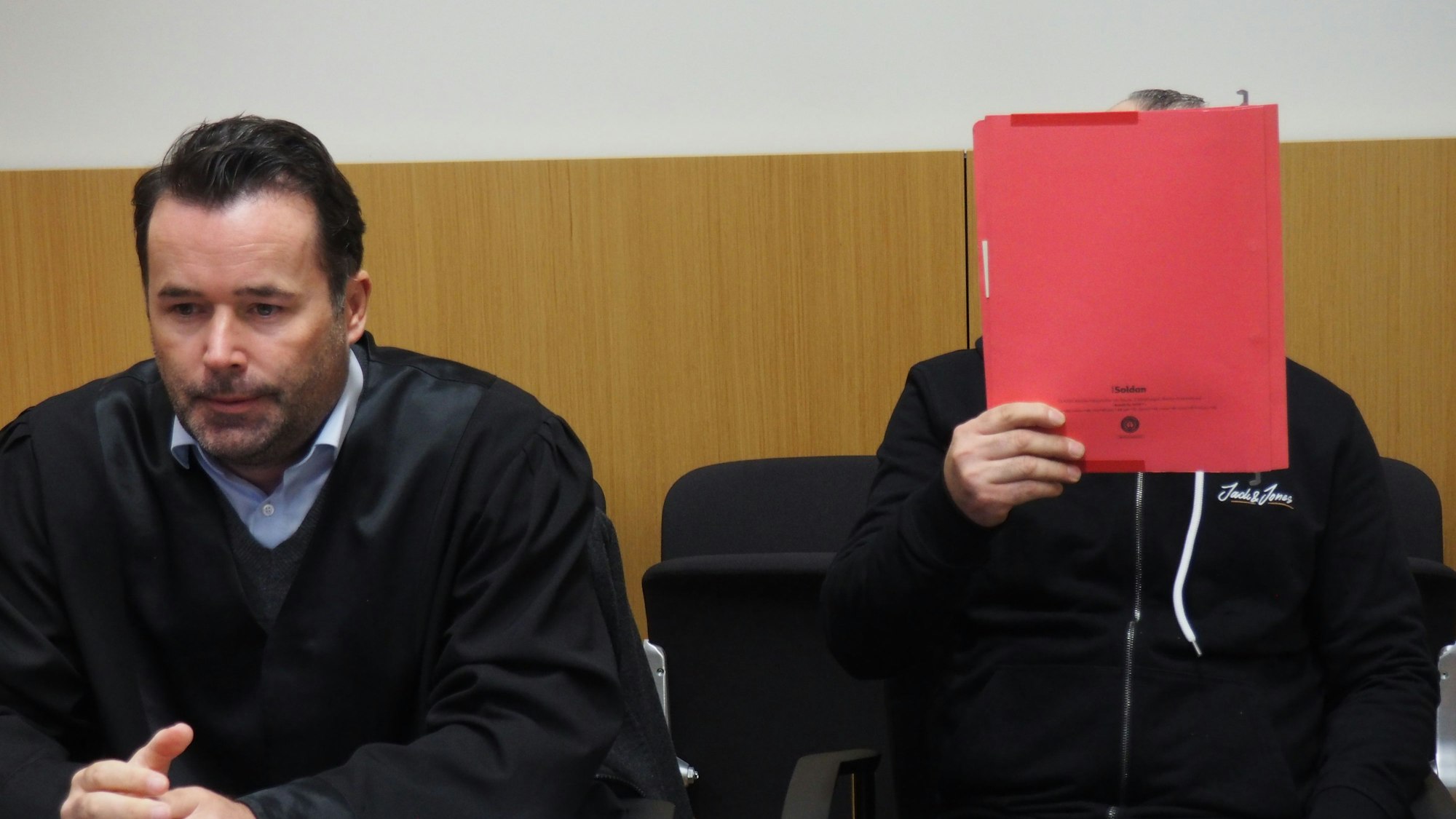 Ahmet R. mit seinem Anwalt am 17. November 2022 im Düsseldorfer Amtsgericht. Der Angeklagte verdeckt sein Gesicht mit einem Aktenordner.