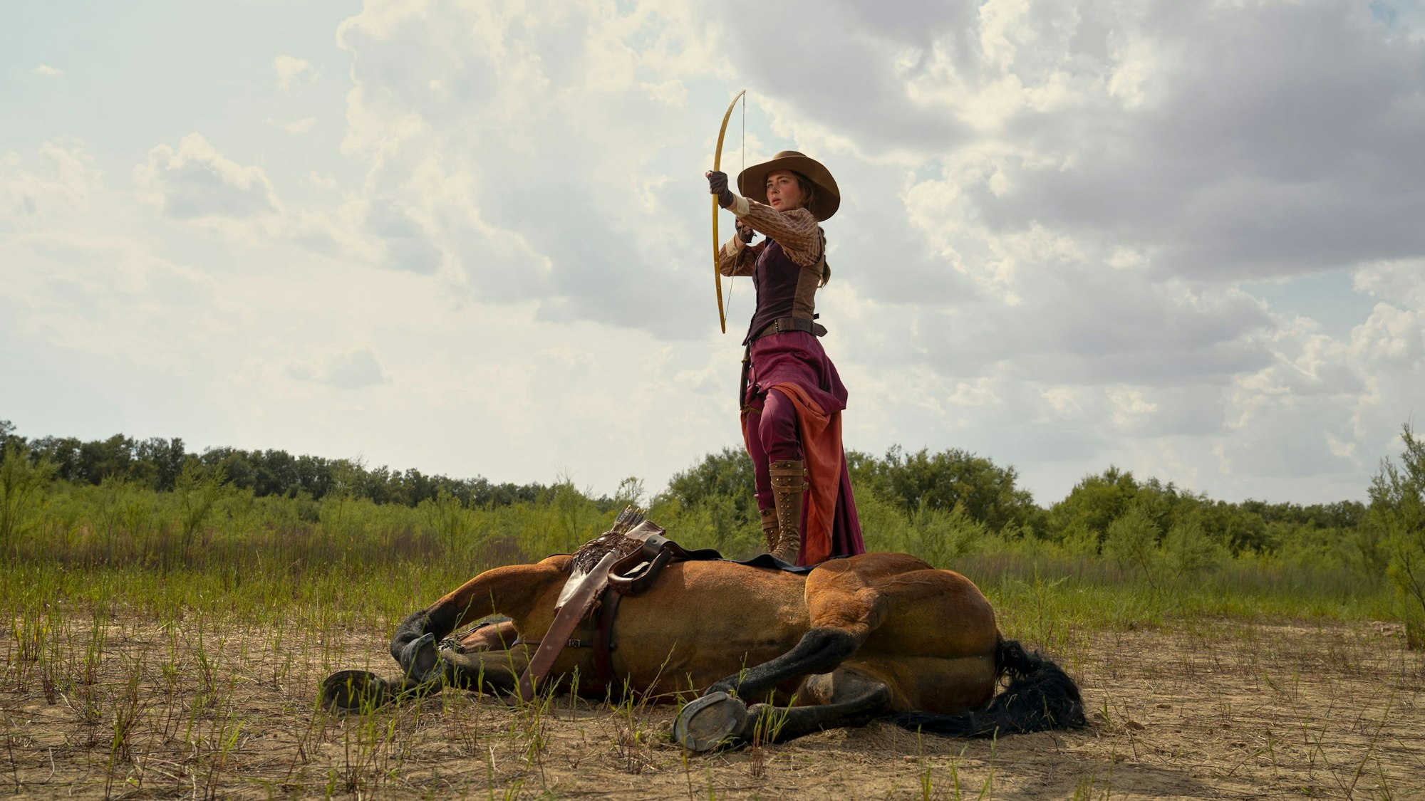 Emily Blunt mit Pfeil und Bogen vor einem liegenden Pferd.