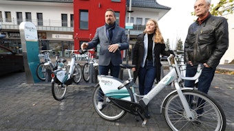 Eine Frau und zwei Männer – Holger Heuser, Kathrin Schmidt und Uwe Weingarten – stehen vor einer Ladestation für E-Bikes und zeigen eines der Fahrräder.