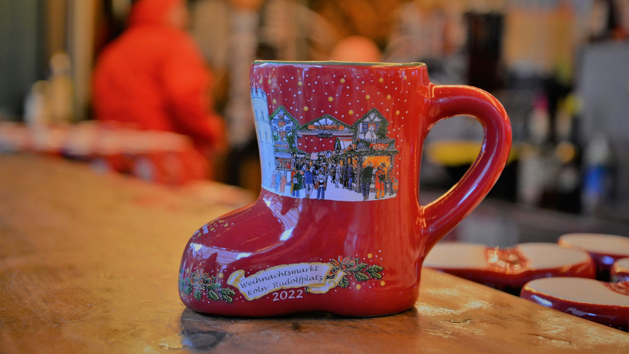 Eine Tasse in Stiefelform steht auf einem Bartisch auf dem Weihnachtsmarkt am Kölner Rudolfplatz.