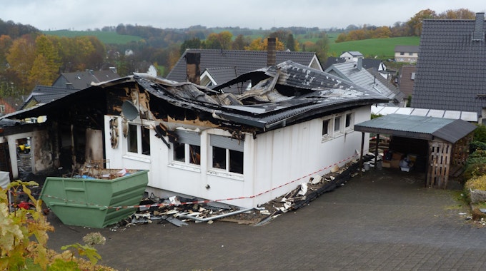 Das Dach eines Einfamilienhauses ist von einem Feuer vernichtet. Vor dem Haus steht ein Schuttcontainer.&nbsp;
