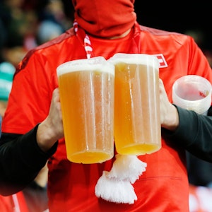 Ein Fan trägt zwei Bier-Becher auf der Tribüne.