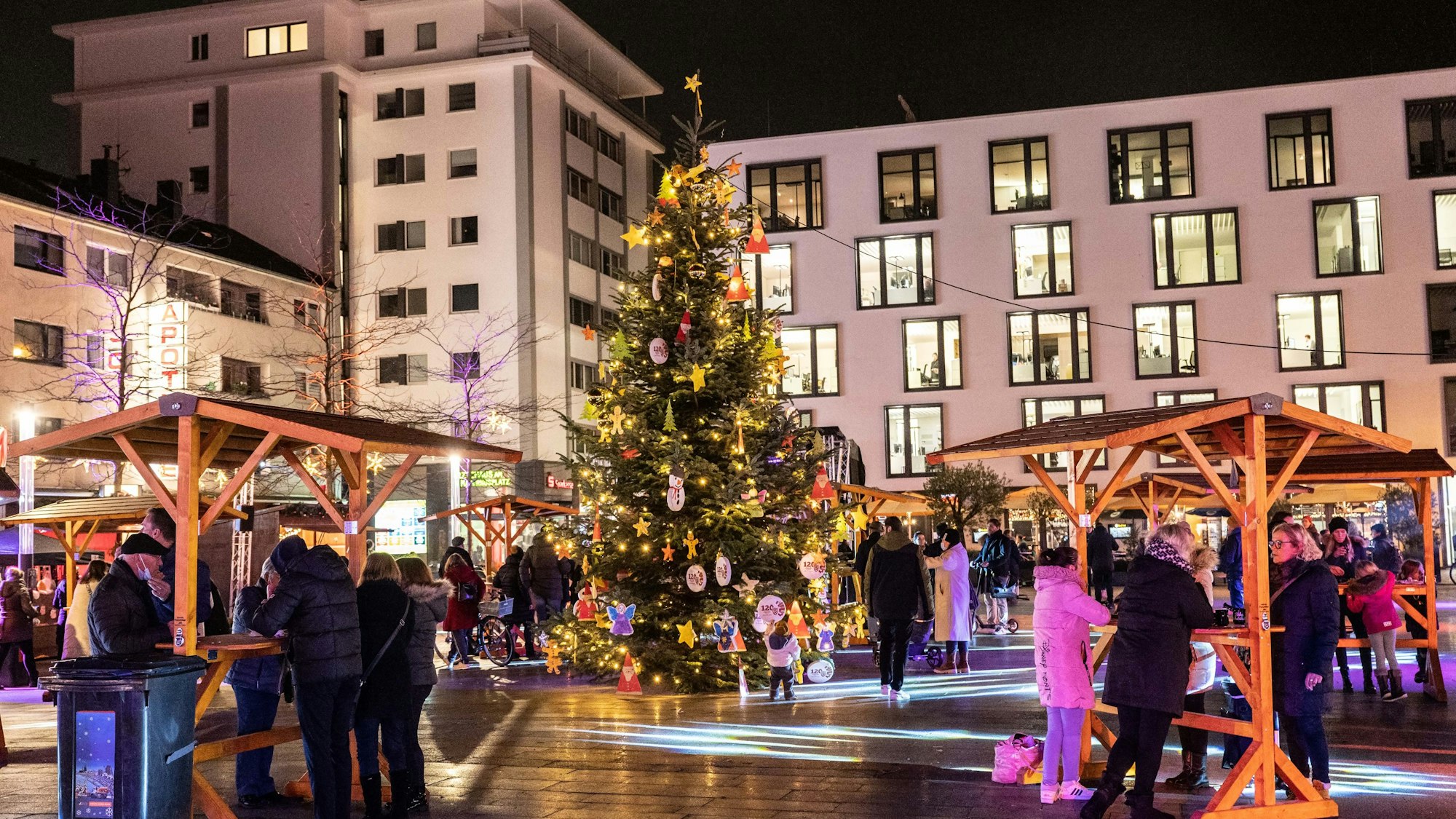 Ein kleiner Weihnachtsmarkt mit überdachten Tischen und einem großen, leuchtenden Weihnachtsbaum