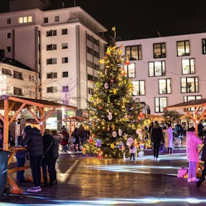In der Mitte des Maternusplatzes steht ein Weihnachtsbaum. Besucher trinken Glühwein.