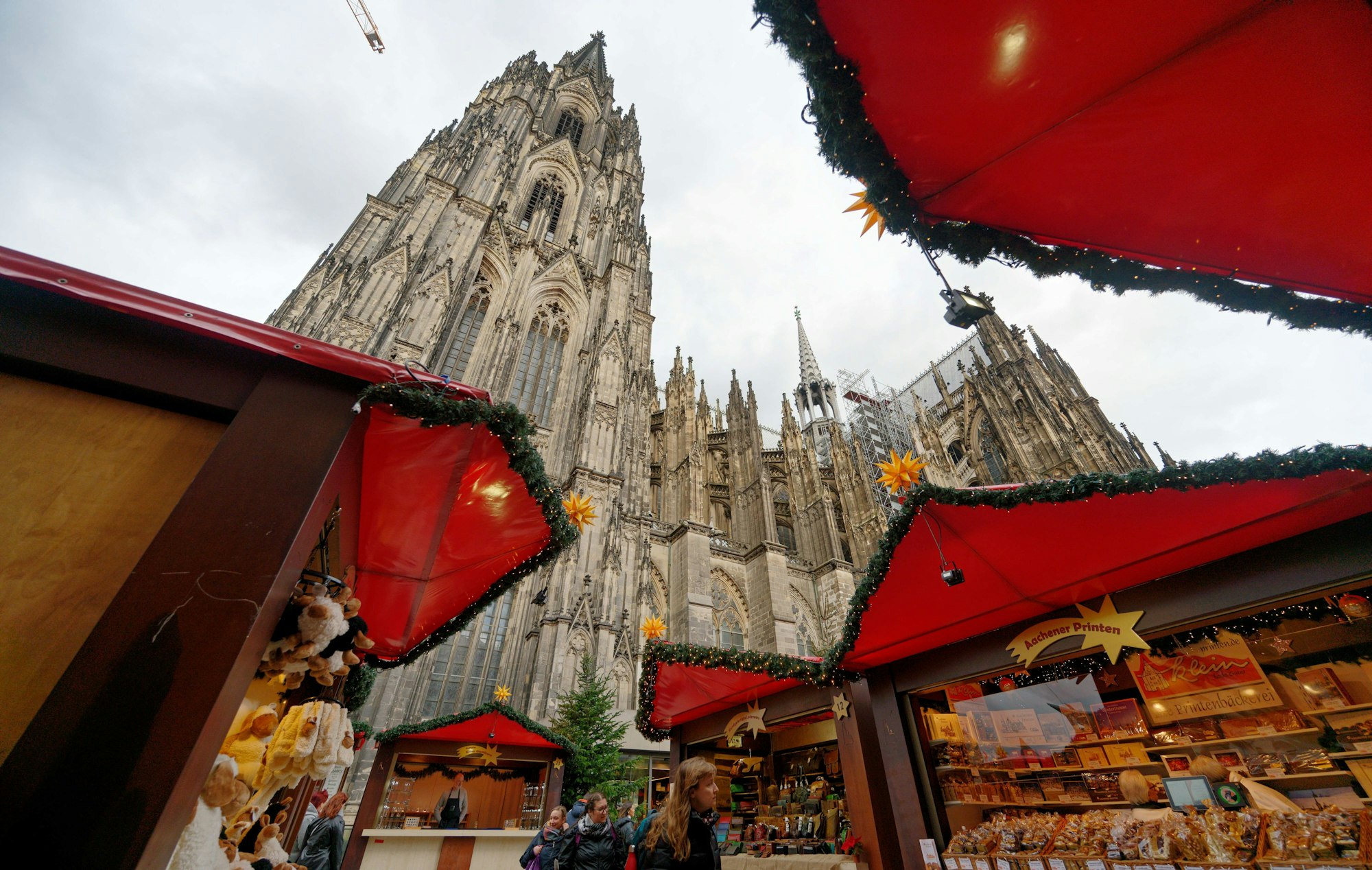Die ersten Besucher gehen durch den Weihnachtsmarkt vor dem Kölner Dom.