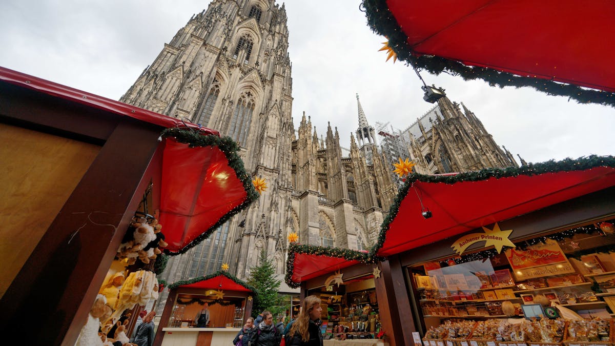 Die ersten Besucher gehen durch den Weihnachtsmarkt vor dem Kölner Dom.