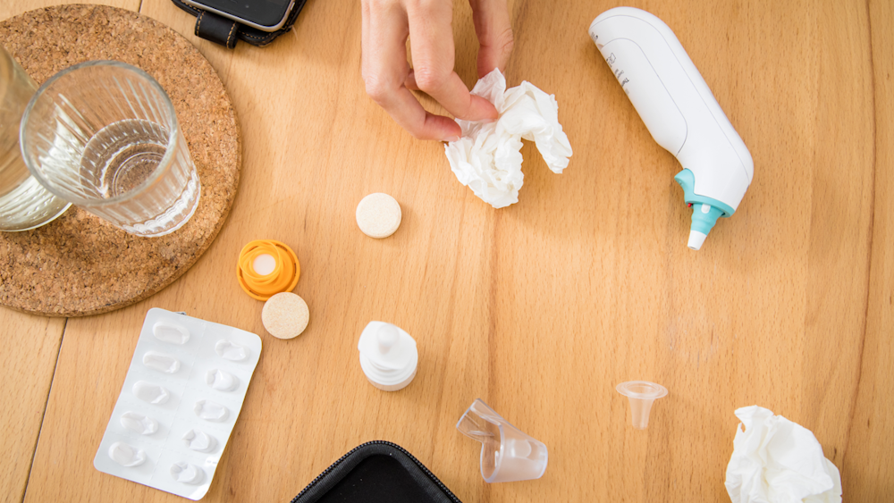 Ein Fiebermessgerät, Taschentücher und Medikamente liegen auf einem Tisch.