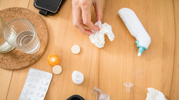Ein Fiebermessgerät, Taschentücher und Medikamente liegen auf einem Tisch.