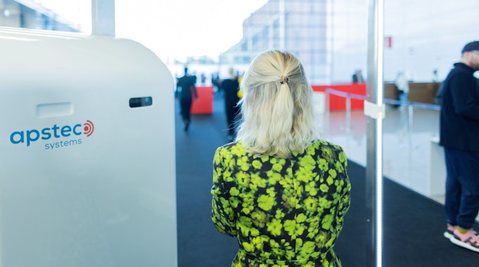 Eine Besucherin der Art Cologne geht im grünen Blumenkleid durch eine Sicherheitskontrolle mit Körperscannern.&nbsp;