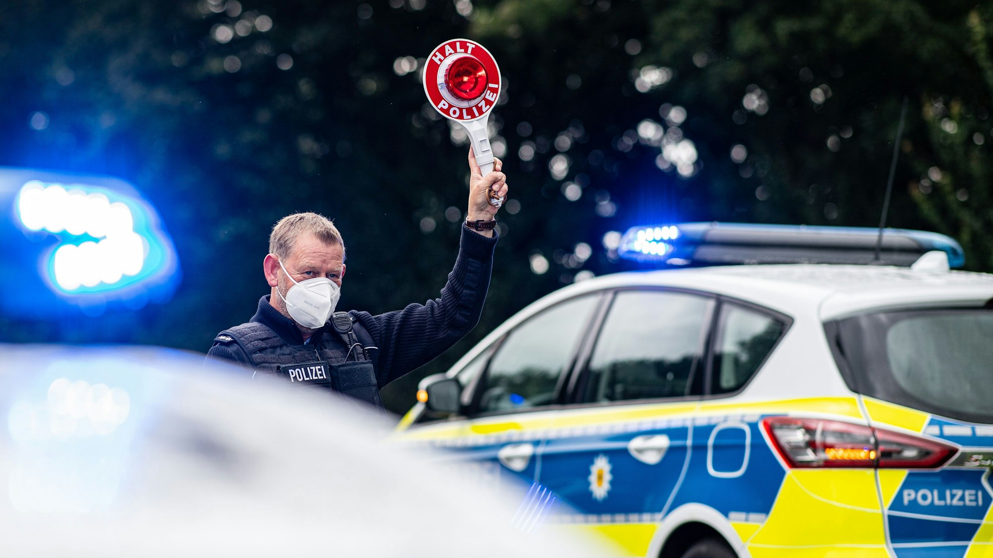 Ein Polizeibeamter steht bei einer Corona-Einreisekontrolle der Bundespolizei an der deutsch-niederländischen Grenze mit einem Polizeianhaltestab und kontrolliert Fahrzeuge im Grenzgebiet.