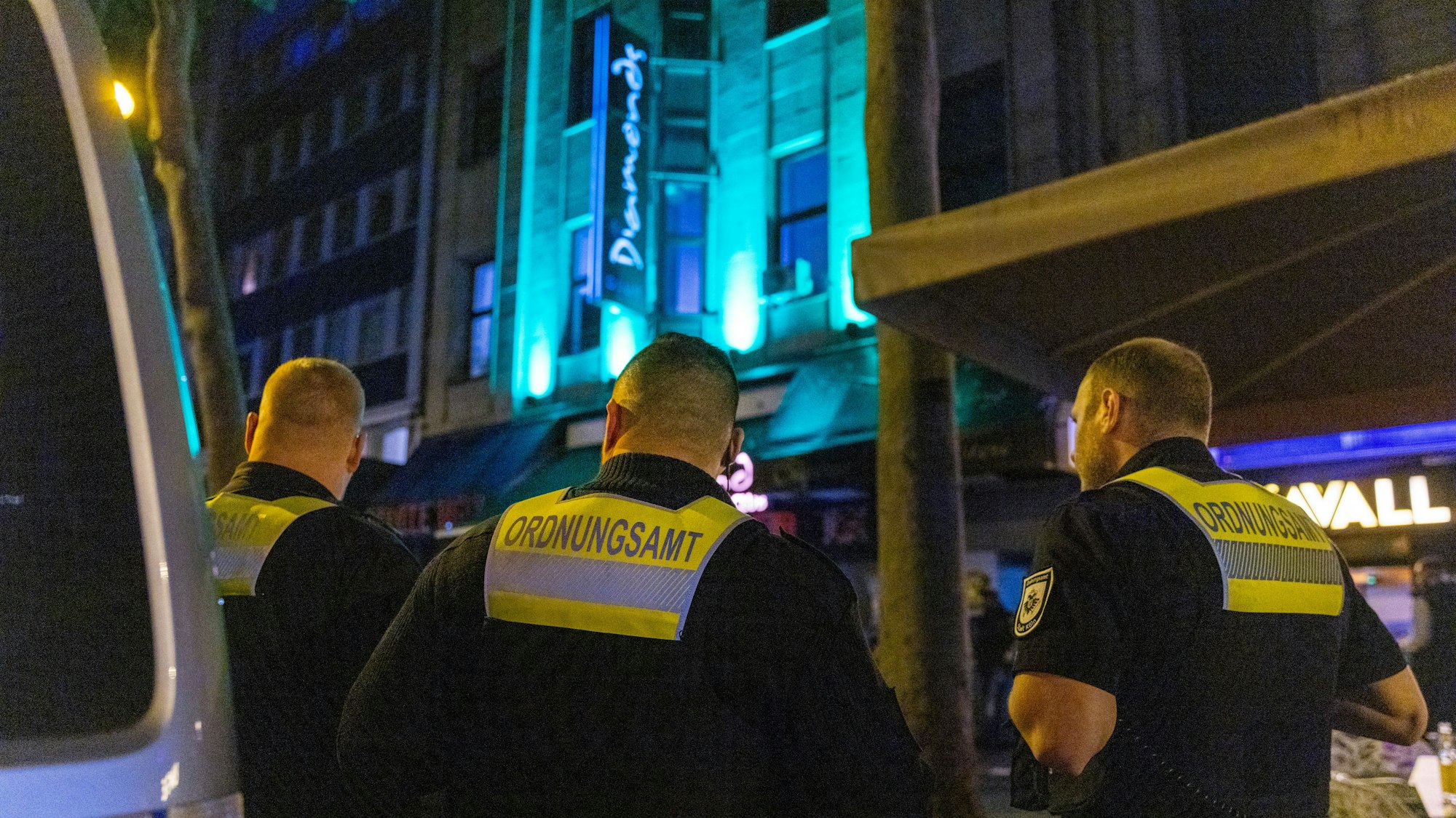 Mitarbeiter des städtischen Ordnungsdienstes stehen nachts vor einem Club in der Kölner Innenstadt.