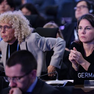 Bundesaußenministerin Annalena Baerbock (Grüne) schaut skeptisch und hat in einem Konferenzsaal Kopfhörer auf. Vor ihr steht ein Schild, auf dem „Germany“ steht.
