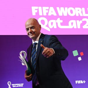 FIFA-Präsident Gianni Infantino steht vor einer Pressewand mit dem Logo der WM 2022 in Katar und hebt den Daumen nach oben.