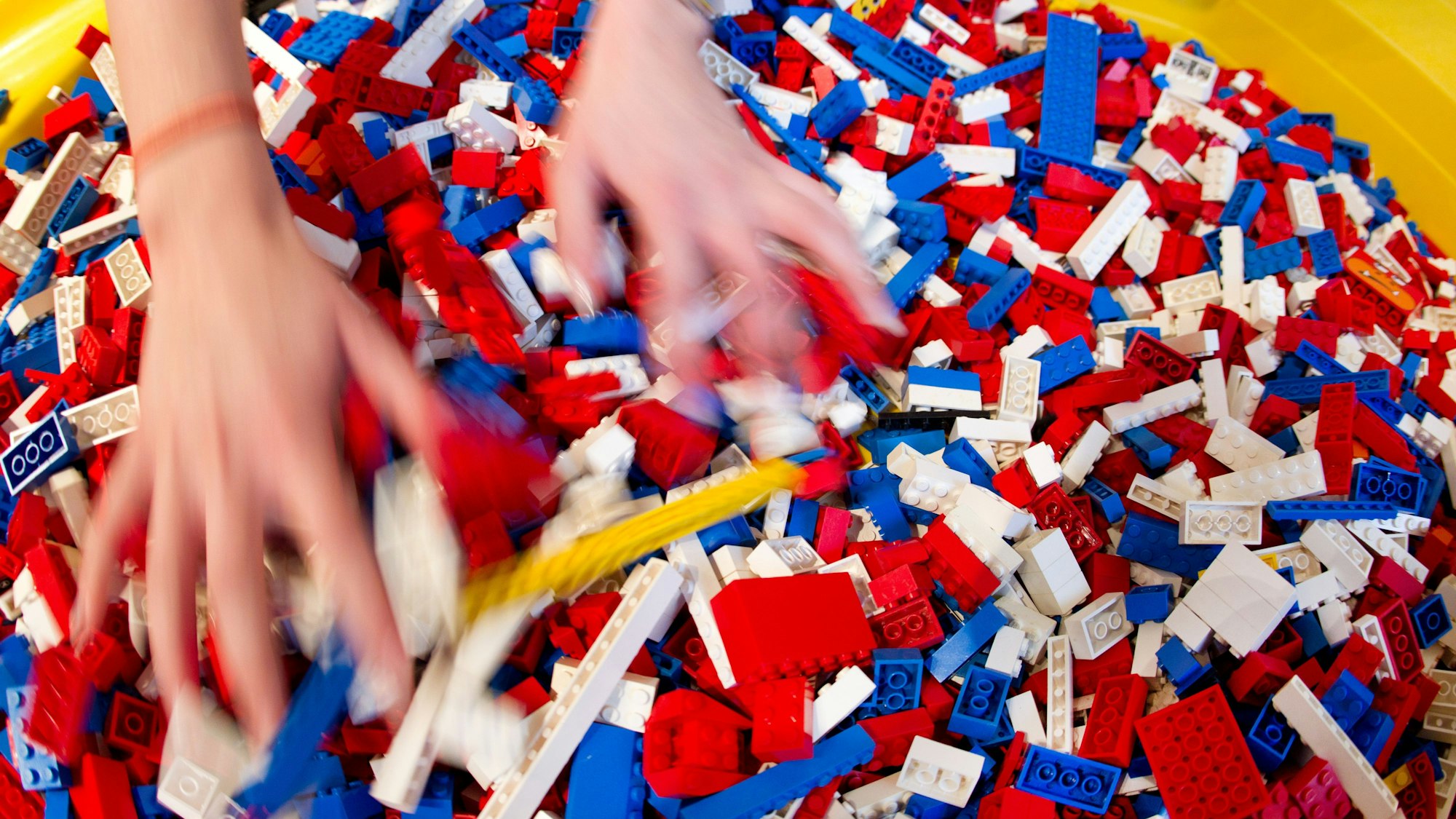 Zwei Hände wühlen in einem bunten Haufen aus Legosteinen.