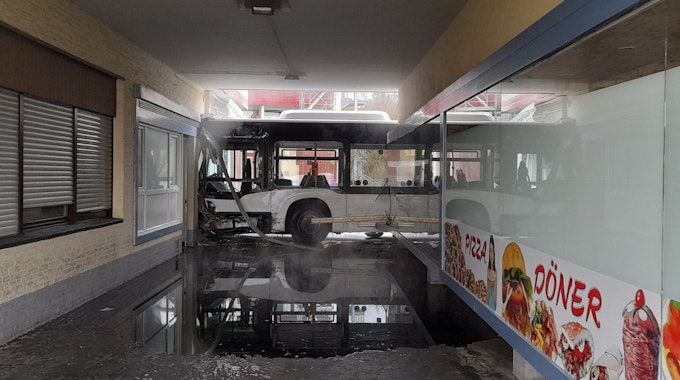 Ein stark beschädigter Bus steht nach einem Unfall an einer ramponierten Ladenzeile.