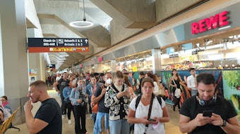 Menschen warten in einer sehr langen Schlange am Flughafen Köln/Bonn für den Check-in und die Sicherheitskontrolle.