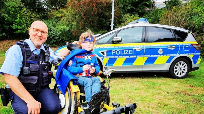 Polizist Dirk Rohde sitzt mit einem schwerkranken Kind auf einem Rasen.