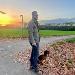 Ein Mann blickt auf ein Feld, sein Hund sitzt neben ihm.